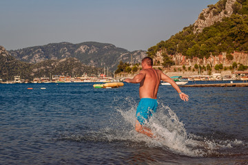 a man in blue bathing shorts runs into the sea
