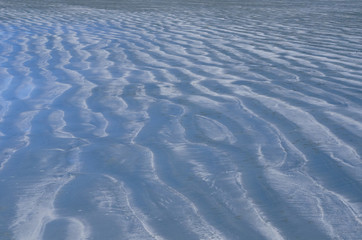 Background and texture photo of blue color sand that have reflection from blue sky and ripple shape from the sea on the beach.