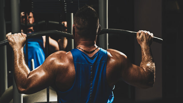 Strong male bodybuilder doing exercise for back with lat pulldown machine in gym, with color imitating social network filter