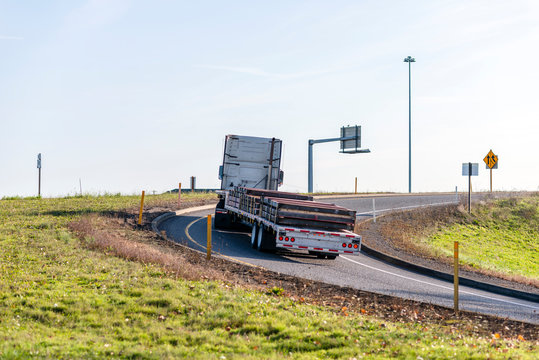 Big Rig Semi Truck Transporting Commercial Cargo Fixed On Flat Bed Semi Trailer And Turning On Highway Going Uphill