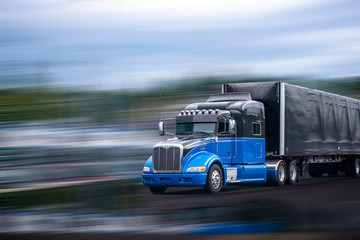 Black and blue stylish big rig semi truck transporting commercial cargo in covered black semi trailer