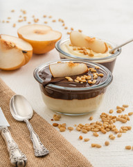 Chocolate and vanilla pudding with pine nuts, and Asian pear slices in a glass bowls on white background. Healthy, tasty, gluten free breakfast