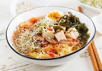 Miso Ramen Asian noodles with cabbage kimchi, seaweed, egg, mushrooms and cheese tofu in bowl on white wooden table. Korean cuisine.