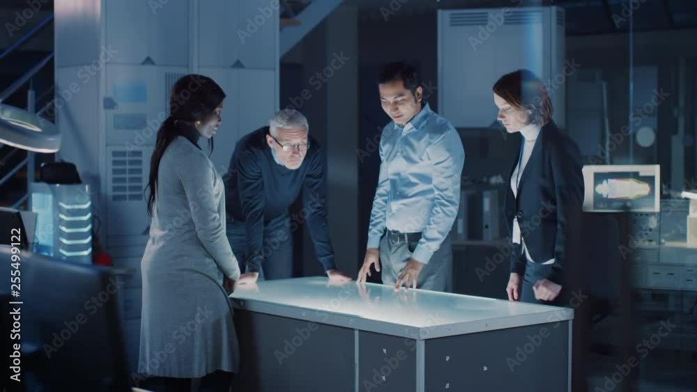 Poster Professionals Meeting in Virtual Reality Content Design Creative Lab: Engineers, Scientists and Game / App Developers Gathered Around Illuminated Interactive Table. Specialists Talking, Gesticulating 