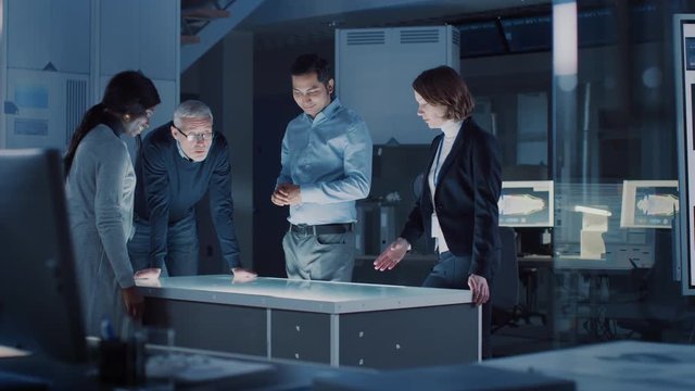 Professionals Meeting in Virtual Reality Content Design Creative Lab: Engineers, Scientists and Game / App Developers Gathered Around Illuminated Interactive Table. Specialists Talking, Gesticulating 