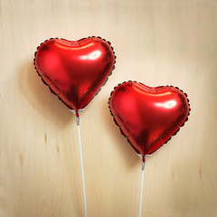 Two heart shape balloons on wooden background.