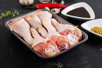 Raw uncooked chicken legs, drumsticks on dark table. Chicken meat with ingredients for cooking.