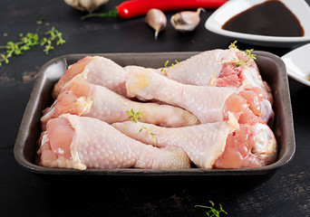Raw uncooked chicken legs, drumsticks on dark table. Chicken meat with ingredients for cooking.