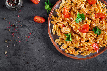 Pasta Fusilli  with tomatoes, chicken meat and parsley on plate on dark table. Top view. Flat lay