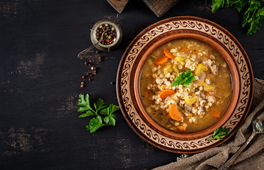 Barley soup with carrots, tomato, celery and meat on a dark background. Top view.