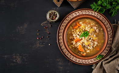 Barley soup with carrots, tomato, celery and meat on a dark background. Top view.