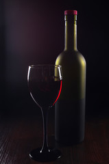A glass of red wine and a bottle on a dark background.