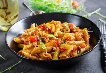 Penne pasta in tomato sauce with meat, tomatoes decorated with pea sprouts on a dark table.