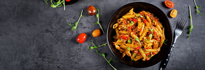 Penne pasta in tomato sauce with meat, tomatoes decorated with pea sprouts on a dark table. Top...
