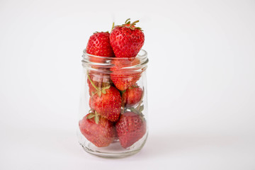 Strawberrys many with both ripe fruit and  not fruit ripe in jar glass and strawberrys all laid are on a white background.
