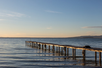 A dog resting on a pier overa a lake, with warm golden hour light