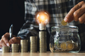 Business man putting coin with light bulb on table for saving bank and account for his money all in finance accounting concept.