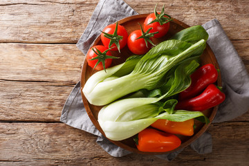 Fresh ingredients baby bok choy, tomatoes and peppers close-up on a wooden table. Horizontal top view