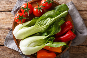 Vegetable assorted fresh baby bok choy, tomatoes and peppers close-up on a plate on a wooden table. Horizontal top view