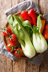 raw healthy baby bok choy, tomatoes and peppers closeup on a plate. Vertical top view