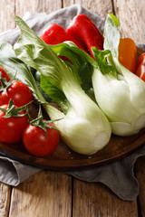 Fresh ingredients baby bok choy, tomatoes and peppers close-up on a wooden table. vertical
