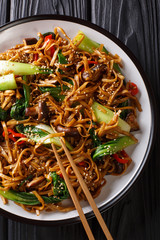 Chinese udon noodles with bok choy, shiitake and pepper close-up on a plate. Vertical top view