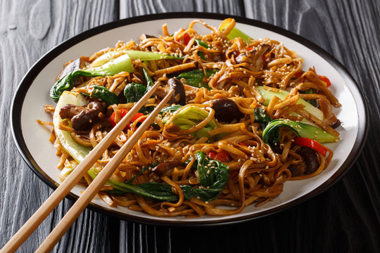 Delicious fried noodles with baby bok choy, shiitake mushrooms, sesame and pepper close-up on a plate. horizontal