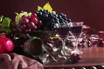 Still-life with two glasses of wine, a bottle and a bunch of grapes on a wooden table