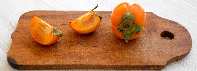 Fresh persimmon on rustic wooden board on white wooden surface, low angle view. Close-up.