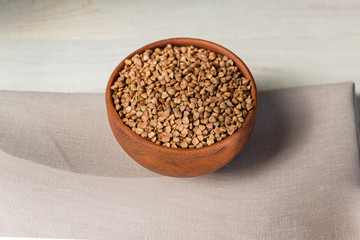 Dry buckwheat in brown clay bowl on wooden table. gluten free grain for healthy diet