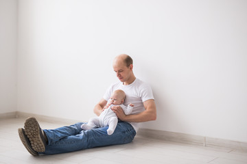 Fototapeta na wymiar Infant, family and fatherhood concept - happy bald father holding baby daughter on knees on white background