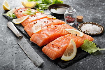 Raw salmon fillet and ingredients for cooking on a dark background.