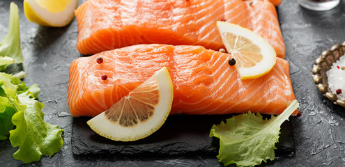 Raw salmon fillet and ingredients for cooking on a dark background.