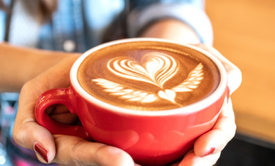 Close-up of a red cup of coffee latte art on woman hand in coffee shop cafe