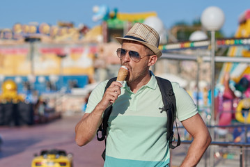 Handsome European man is eating ice-cream in the Luna Park. He is on his holidays.
