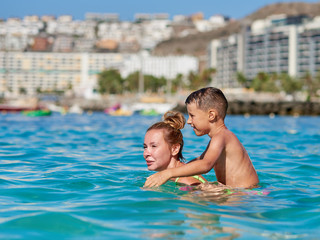 Attractive European woman hand her son swimming in the ocean during their vacations.