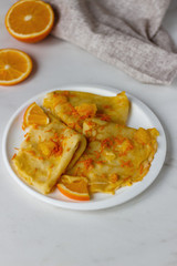Traditional French crepes Suzette with orange sauce on white plate over marble background.copyspace for your text