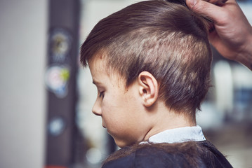 The portrait of a cute European boy in a barbershop. He is getting his new hairstyle...
