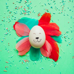 Bunny rabbit smiling face made of painted egg lay with colorful feathers on bright background. Easter minimal concept. Flat lay.