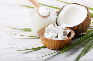 Coconut shell hard oil in glass jar and coconut meat pieces in bowl on white wooden table