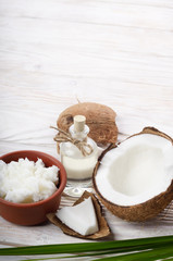 Background of coconut, coconut shell, oil in clay bowl and glass jar on white wooden table