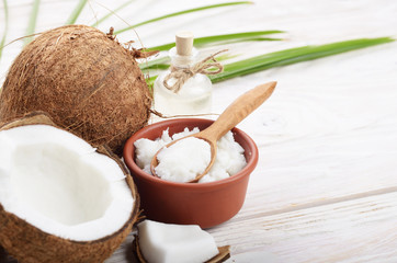 Background of coconut, coconut shell, oil in clay bowl and glass jar and spoon on white wooden table