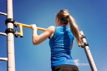 young athletic fitness woman working out at outdoor gym doing pull ups at sunrise