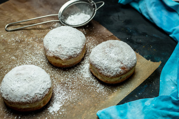fresh, homemade fluffy donuts with powdered sugar on baking paper, on the kitchen table