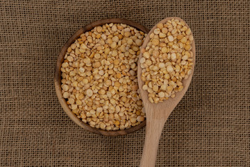 Raw yellow plate with wooden spoon and spoon against the background of burlap texture