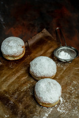 fresh, homemade fluffy donuts with powdered sugar on baking paper, on the kitchen table