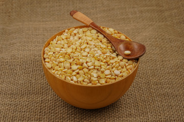 Raw yellow plate with wooden spoon and spoon against the background of burlap texture