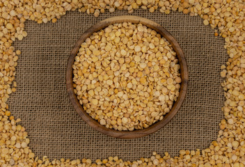 Raw yellow split peas in a wooden plate on a background of pea texture