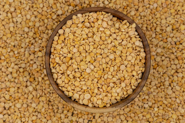 Raw yellow split peas in a wooden plate on a background of pea texture