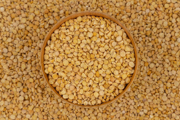Raw yellow split peas in a wooden plate on a background of pea texture